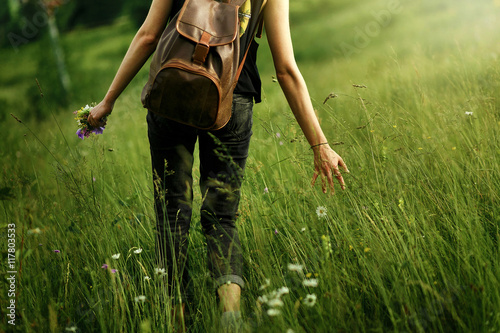 woman traveler walking among grass in meadow and holding in hand