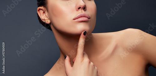 Close-up lips, neck and shoulder of young girl, touching her chic over grey background photo
