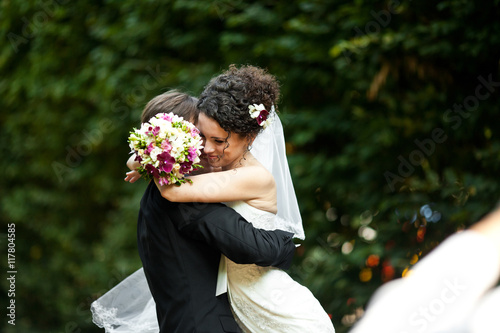 Happy bride twines her hands around groom's neck while he whirls photo