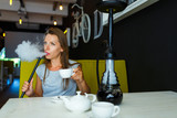 Beautiful woman smoking a hookah and drinking tea in a cafe