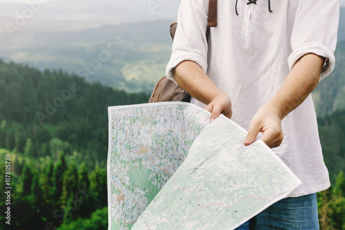 stylish hipster traveler man holding map and exploring at top of