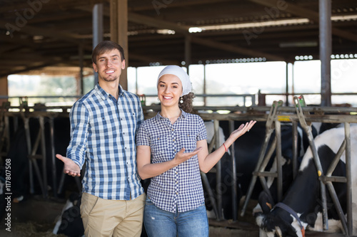 Cheerful man and woman farmers standing with in the cow hangar