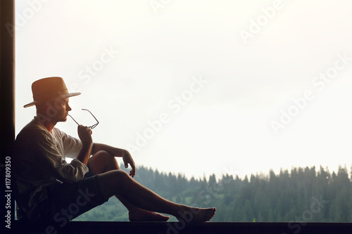 man sitting relaxing and thinking with glasses in hand on porch
