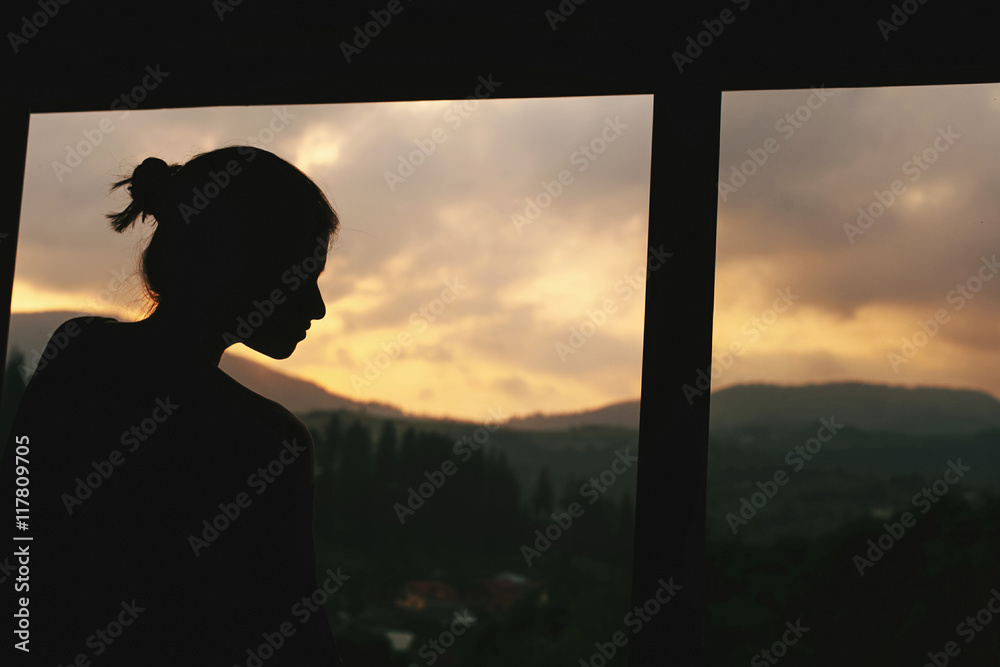 Fototapeta premium silhouette of hipster woman in wooden cottage window with view