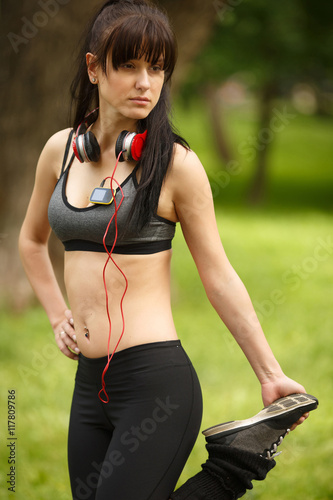 Athletic brunette woman with headphones in tracksuit stretching leg