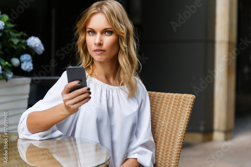 Portrait of blonde woman sitting in cafe with smartphone