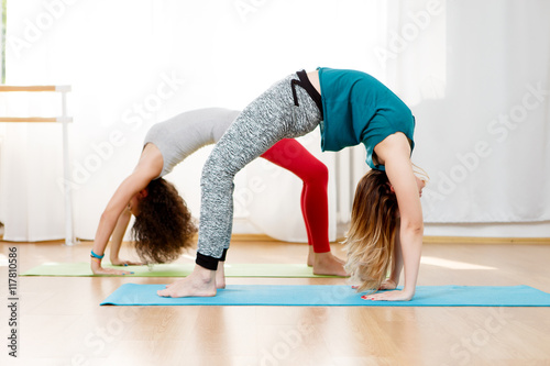 Flexible young women practice chakrasana asana in yoga studio photo