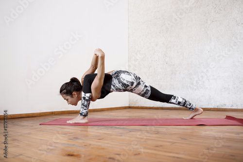 Young beautiful athletic girl practicing indoor yoga streching asana on red mat.