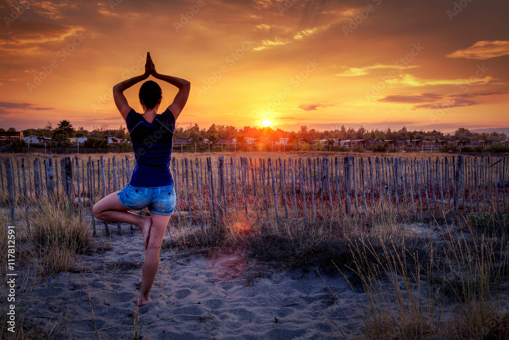 Femme faisant du yoga face au coucher du soleil: posture de l'arbre -  Vriksasana Stock Photo