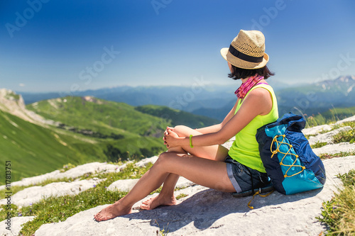Unrecognizable young woman sitting on a rock with backpack and looking to the horizon