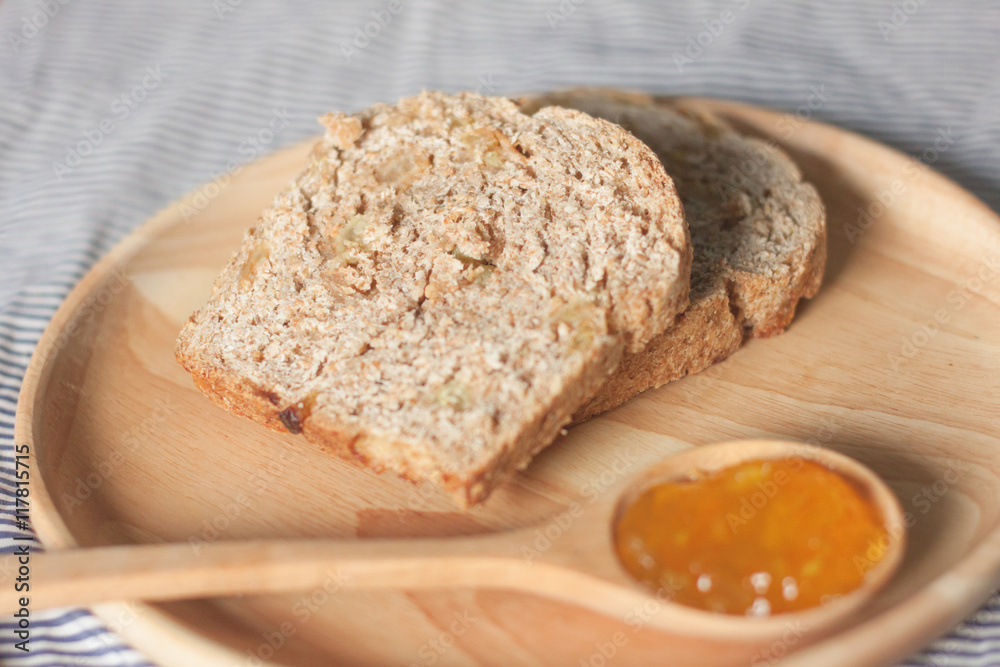 whole wheat bread and orange jam are on the wooden plate