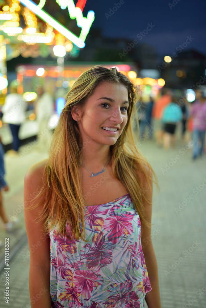 Happy young girl in floral jumpsuit against of bright carousel Happy young girl in floral jumpsuit against of bright carousel