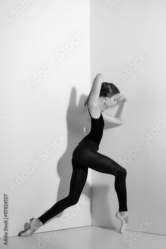 Ballerina in black outfit posing on pointe shoes, studio background.