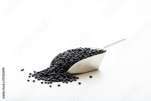 Raw black lentils in a metallic scoop on white background