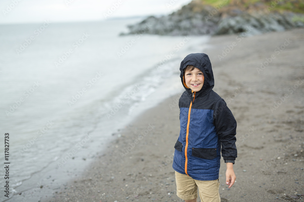 boy enjoying the rain and having fun outside on the beach  a gray rainy