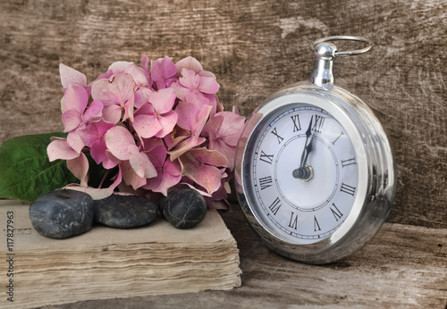 pendule rétro marquant midi ou minuit, fleur d'hortensia et vieux livre  sur fond bois 