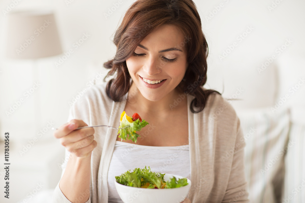 smiling young woman eating salad at home