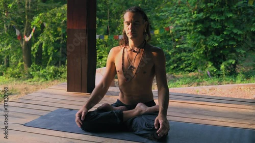 A man sitting on a rug on a wooden platform in the park is set on meditation. photo