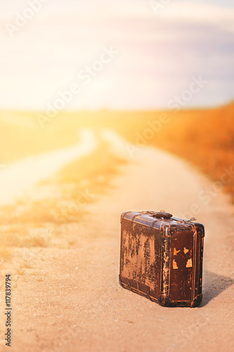 Abandoned, forsaken  vintage luggage suitcase on the asphalt road in the summer sun shine in the nature and beautiful light
