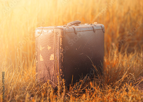 Forsaken abandoned old vintage luggage suitcase on the field summer sun light