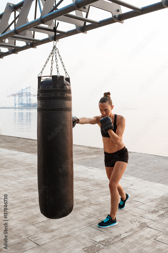 Young beautiful sportive girl training boxing at seaside.