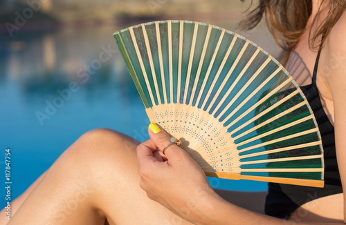 Girl in bikini holding a hand fan by the pool