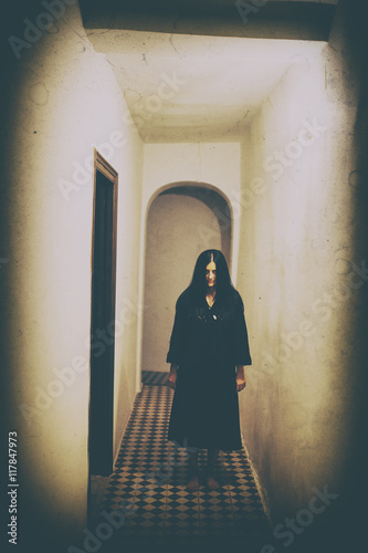 Horror scene of black-haired woman in black in hallway photo