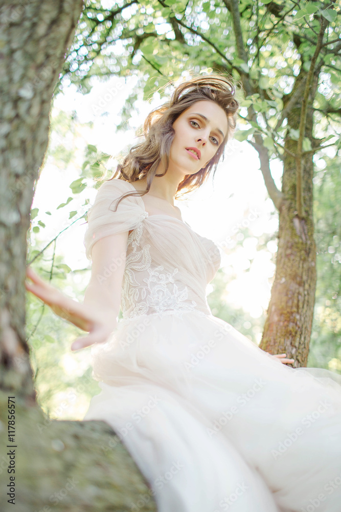 Young bride in beautiful wedding dress sitting on tree outdoors Young bride in beautiful wedding dress sitting on tree outdoors