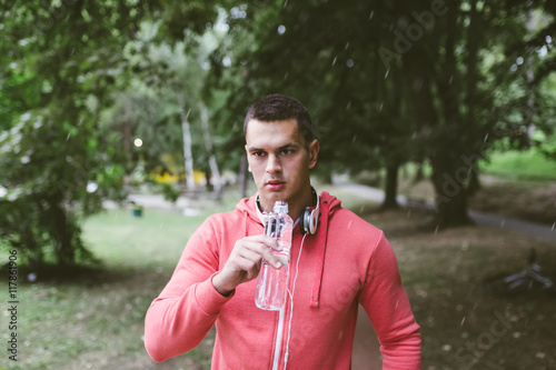 Young handsome man jogging in a park and drinking fresh water.