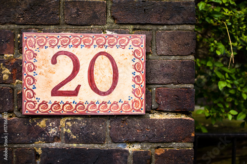 Hand painted number 20 (twenty) tile on brick wall. House number 