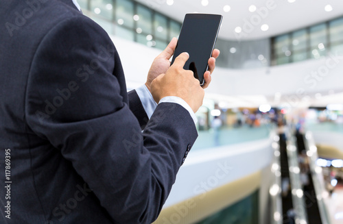 isolated business man hold the smartphone on shopping mall background 