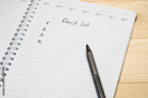 Checklist on notebook page with pen on wood background