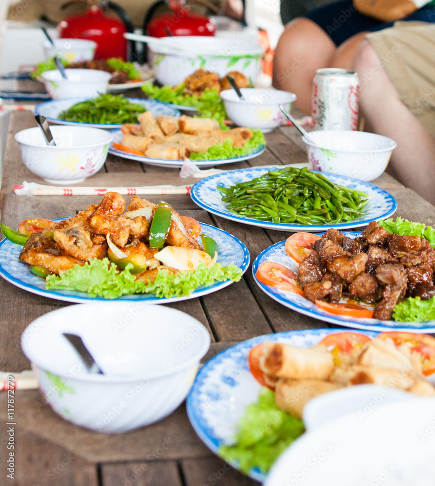 Asian cooked meal range of meats, vegetables and salad dishes and bowls spread out on table Asian cooked meal range of meats, vegetables and salad dishes and bowls spread out on table