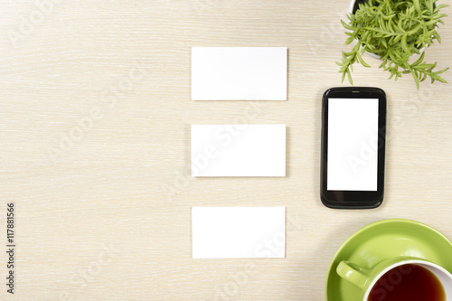 Business card blank, smartphone or tablet pc, flower and coffee cup at office desk table top view. Corporate stationery branding mock-up