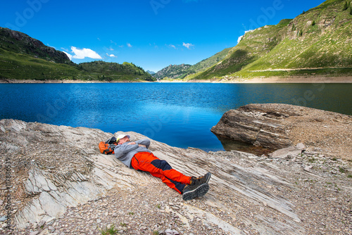Man rests and sleeps near a mountain lake during an alpine hikin