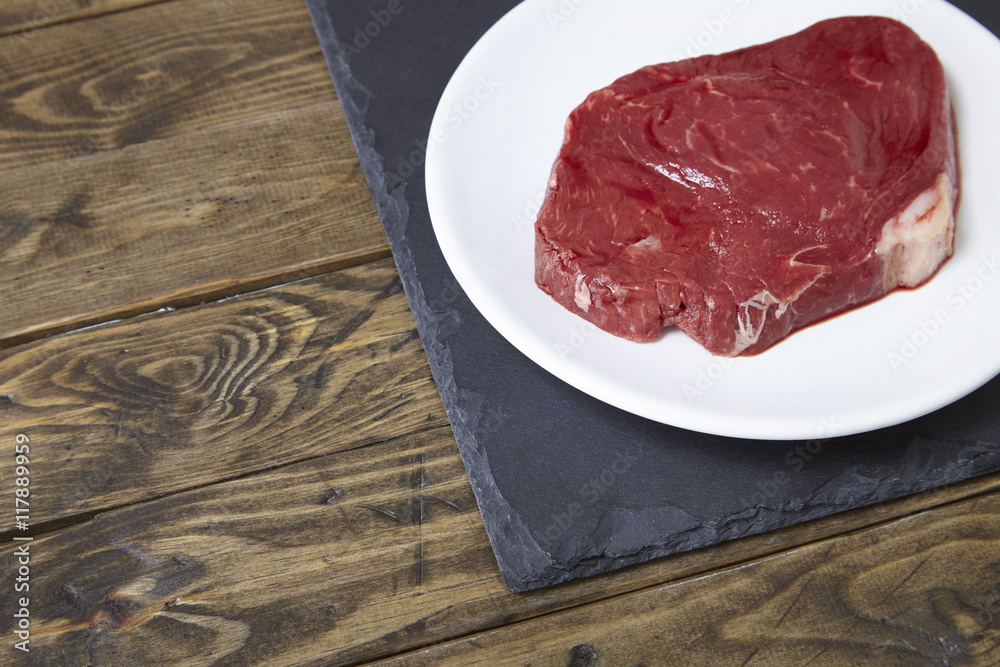 A uncooked fillet of steak meat on a distressed wooden counter top background forming a page border