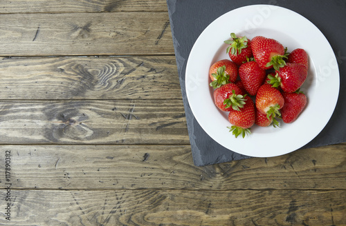 An aerial view of a bowl of ripe British strawberries on a rustic table top background forming a page border