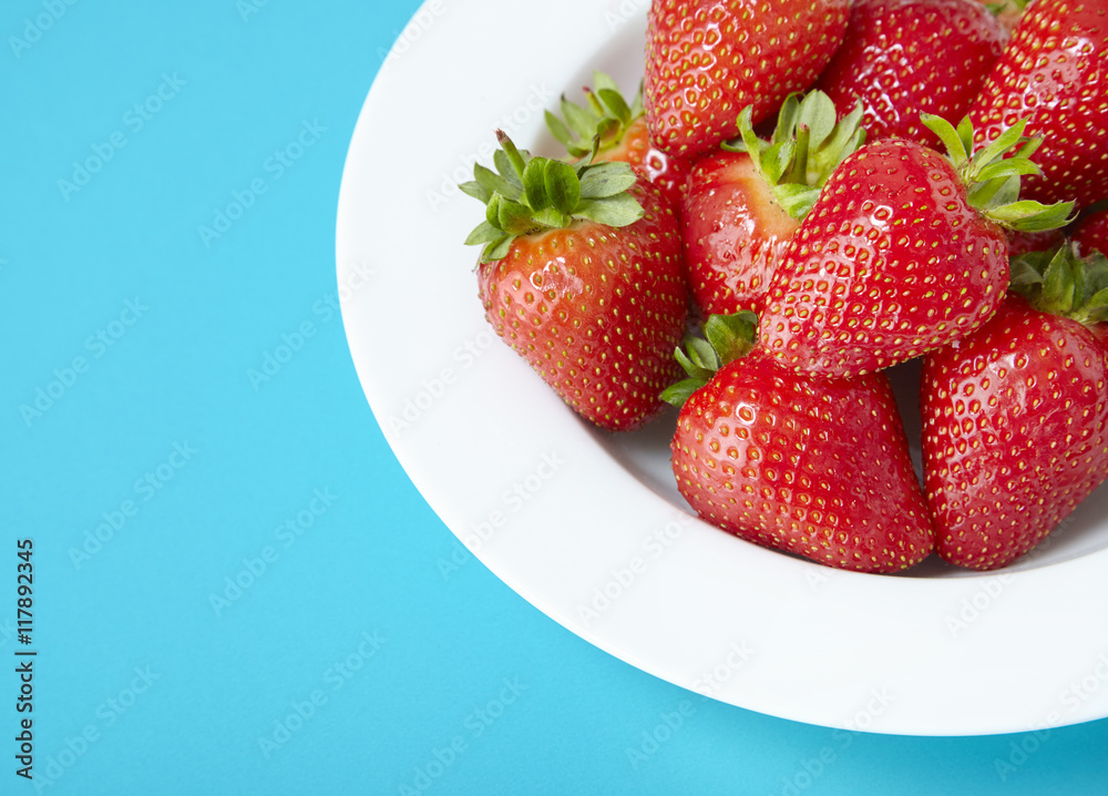 A bowl of whole ripe strawberries on a bright blue background A bowl of whole ripe strawberries on a bright blue background