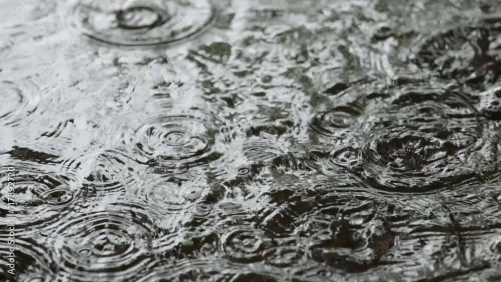 Closeup of rain drops falling in the puddles on the road Closeup of rain drops falling in the puddles on the road