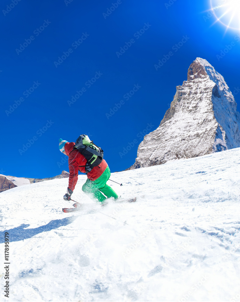 Skier skiing downhill in high mountains against sunshine