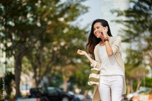 Vietnamese cheerful young woman walking along the street and calling on phone photo