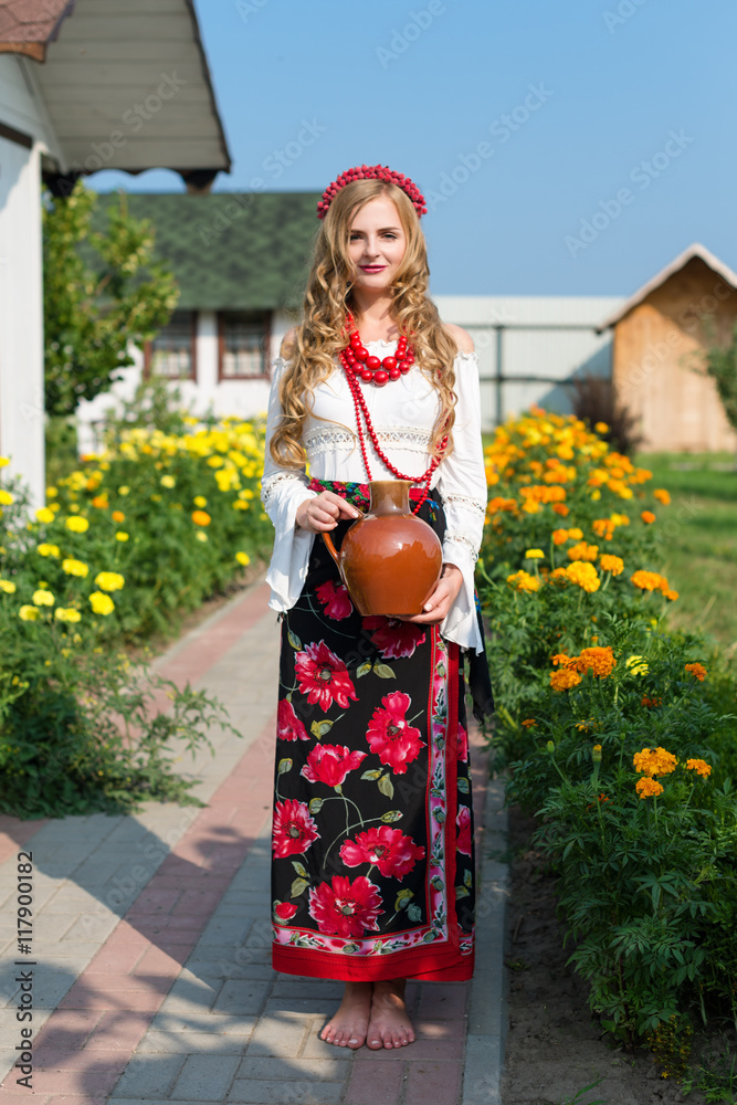 Obraz premium woman in national ukrainian traditional costume holding a clay jug and welcoming guests