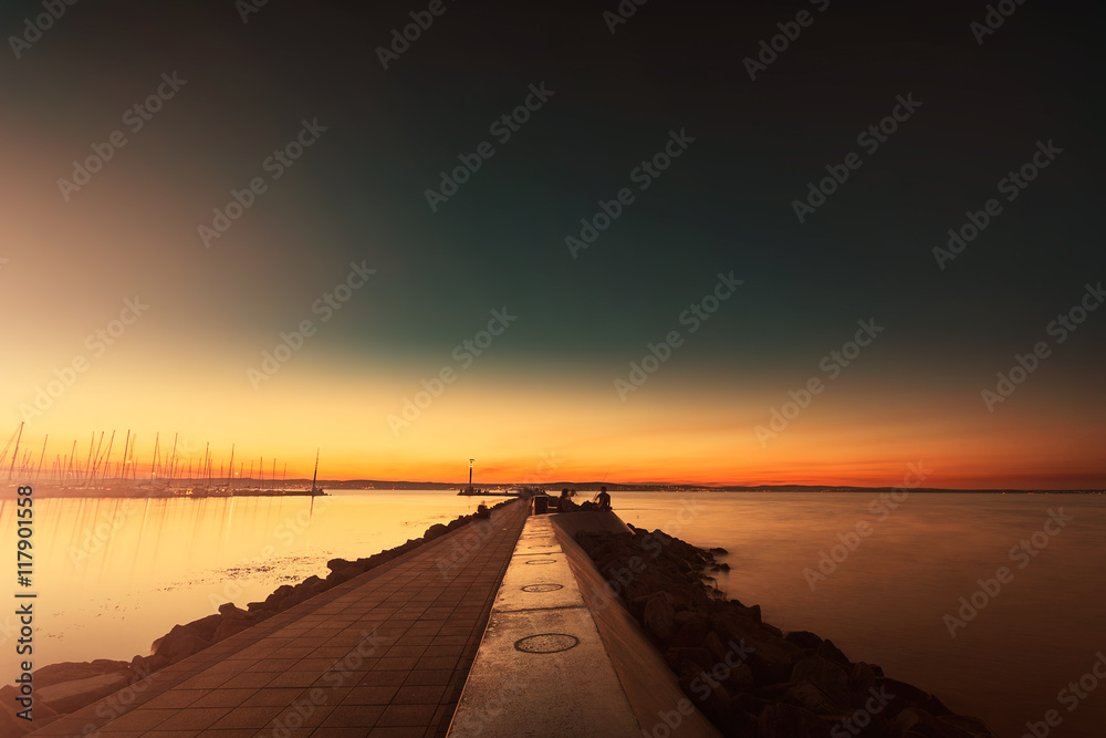 Pier at sunset by the lake Balaton Hungary with fishing people silhouette and mood sunlight