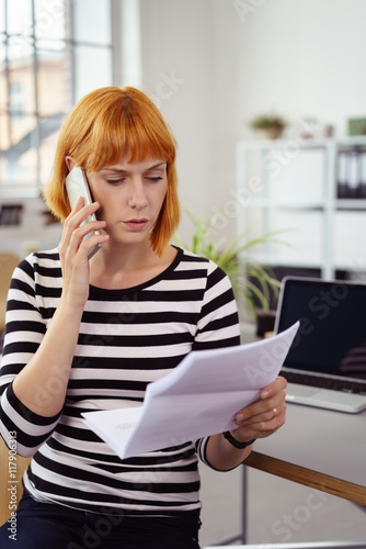 frau im büro schaut wütend auf einen brief und telefoniert