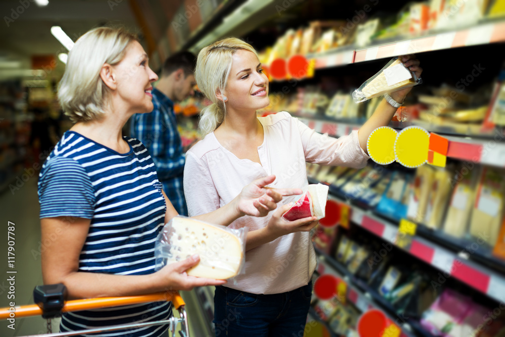 Adult girl with senior mother in cheese section of supermarket