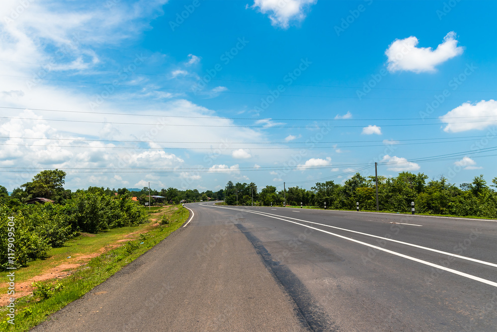 Asphalt road through the countryside and clouds on blue sky in summer