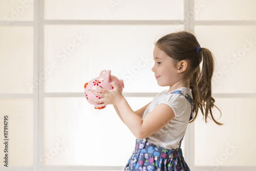 Portrait of happy young little girl looking at her pink piggy bank. Education, school and money saving concept. Junior Savings Account concept