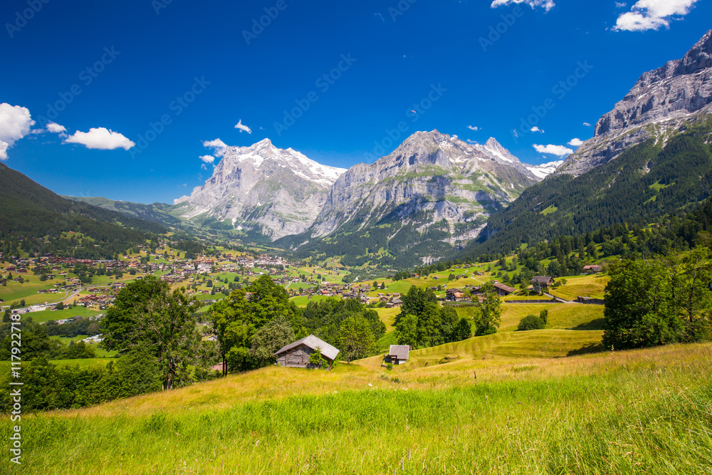 View to famous Grindelwald valley, green forest, Alps chalets and Swiss Alps (Schreckhorn, Berglistock and Wetterhorn) in the background, Berner Oberland, Switzerland, Europe. 