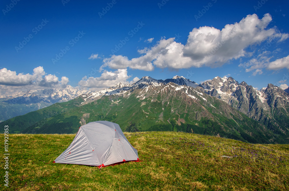 gray tent in grass on background of mountains and rocks
