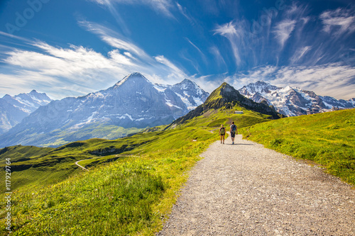 Young couple hiking in panorama trail leading to Kleine Scheidegg from Mannlichen with Eiger, Monch and Jungfrau mountain (Swiss Alps) in the background, Berner Oberland, Grindelwald, Switzerland. 